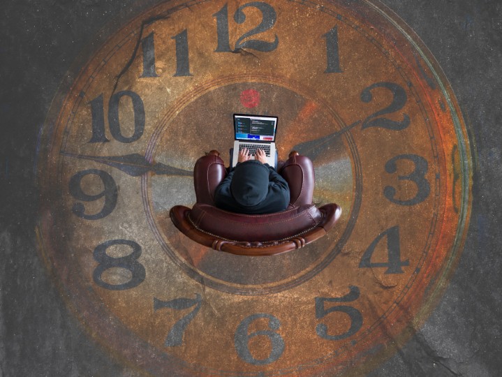 A person is sitting on top of a giant clock on the floor while holding a laptop