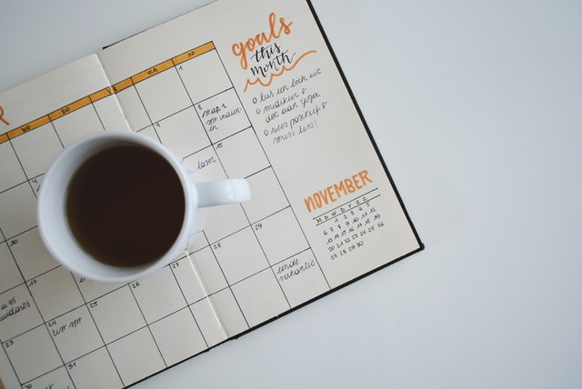 An open calendar with a cup of coffee on top of it as scheduling really helps in distance learning. 