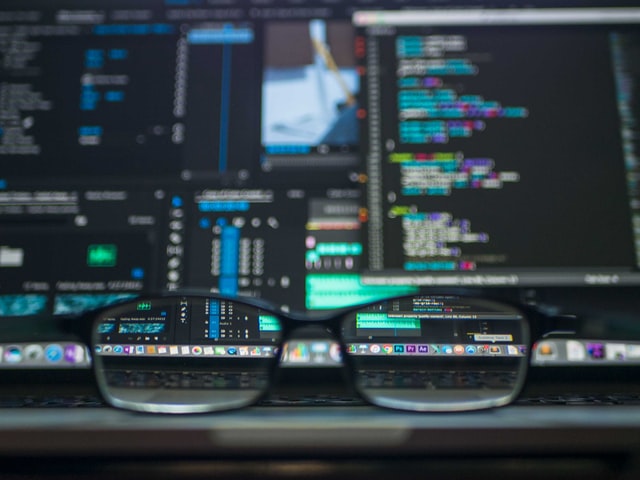 A programmer's screens with coding being visible through the glasses who are laid on the desk