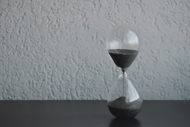 An emptying hourglass on a table to measure time which is part of iron triangle in project management.