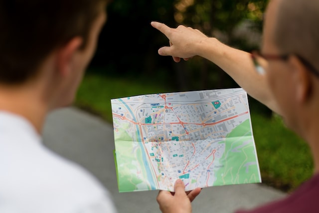 A travel business guide holds a city map and gives direction to someone with his finger pointed. 