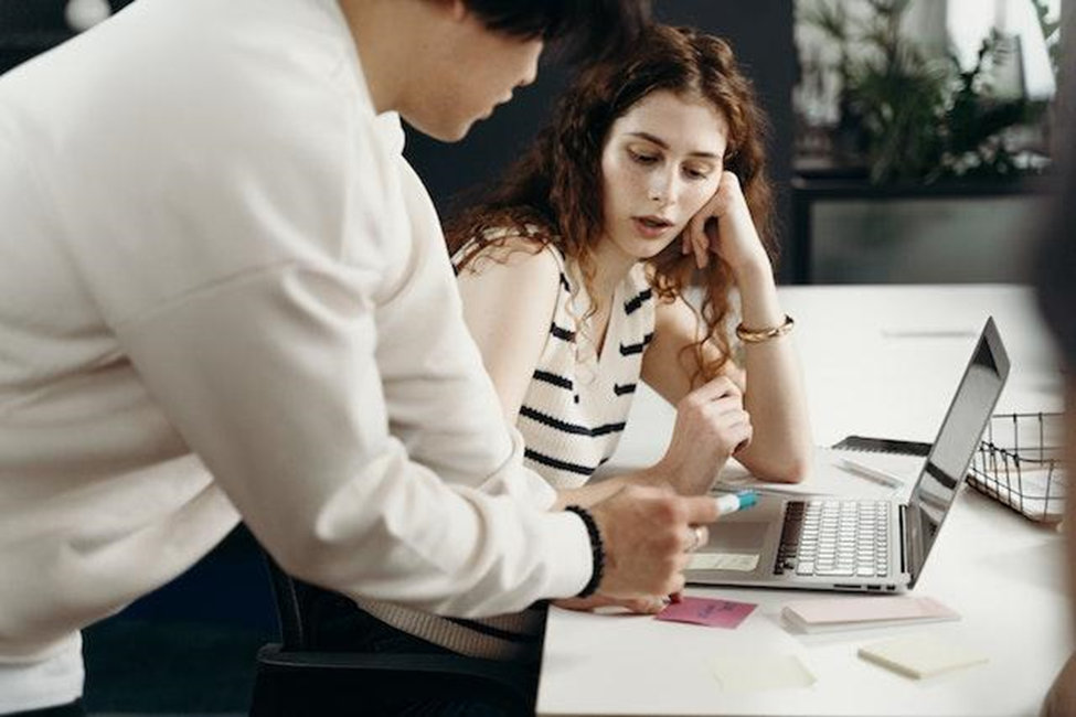 A woman talking to a man while sitting at the table in front of the laptop