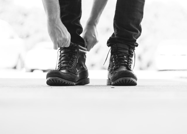 A black and white picture with man putting on his boots.