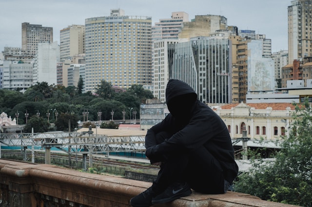 A hacker in black is sitting on a railing. 