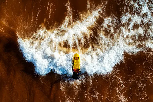 An aerial shot of a search and rescue person inside the sea on top of a red and yellow board. 